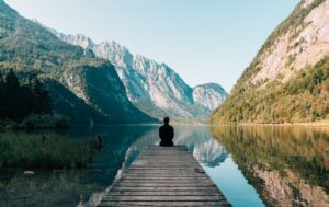 Person sitting at the edge of a peer surrounded by water and mountains | Hero image for Overcoming Insecurity for SUD professionals